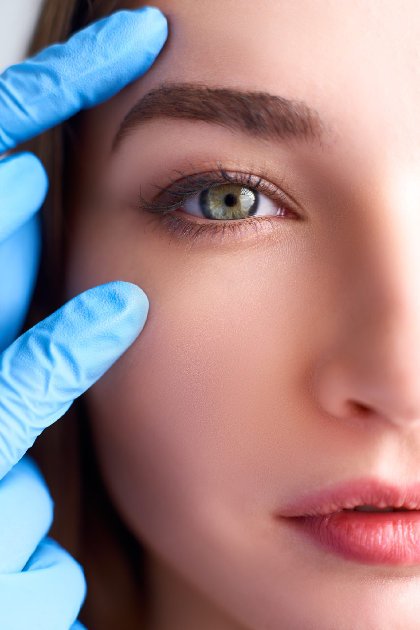 Beautician doctor hands in gloves touching female face. Upper eyelid reduction, double eye lid removal plastic surgery concept. Ophthalmologist or oculist checks healthy vision in green eyesight.